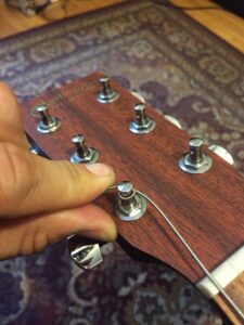 Wound guitar strings spiral around silver tuning pegs on a wooden headstock.