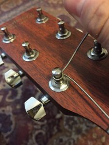 A hand adjusting a wound guitar string on a wooden headstock with tuning pegs.