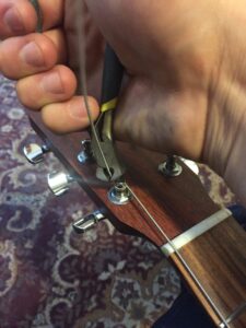 A hand holding a guitar with a wound metal string visible on the headstock.