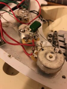 Guitar circuit components including a potentiometer with colored wires soldered to its terminals.