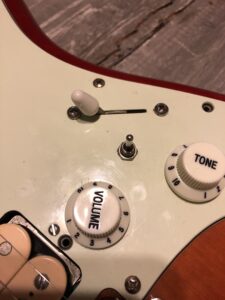 A pickup selector switch positioned above volume and tone knobs on a guitar.