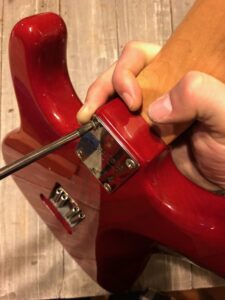 A person removing the neck from a red electric guitar by hand.