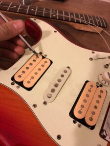 Hand holding multimeter probe to test toggle switch on red and white guitar.