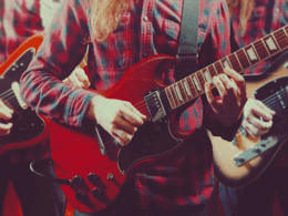A musician in red plaid shirt plays a red electric guitar.