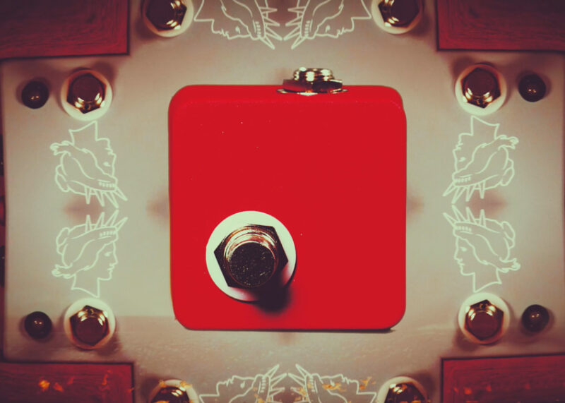 Multiple JHS pedals arranged symmetrically around a central red pedal on a reflective surface.