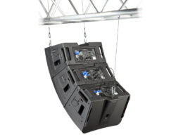 Three black QSC line array speakers suspended from a white metal truss above.