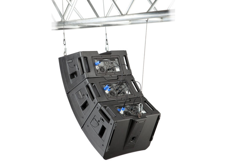 Three black QSC line array speakers suspended from a white metal truss above.