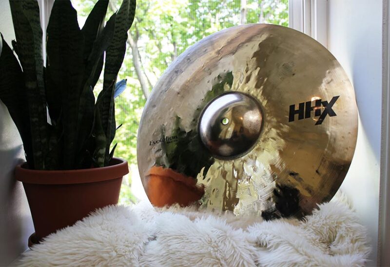 An HHX cymbal rests against a potted plant by a window.