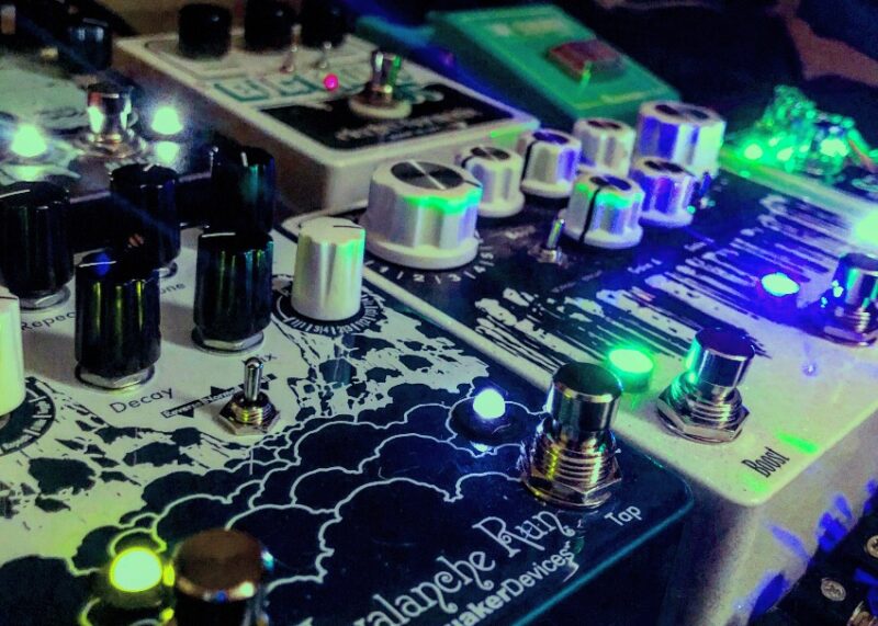 Close-up of DJ equipment with illuminated knobs and faders glowing green and blue.