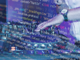 A programmer's hand adjusts DJ turntables while code projections overlay the equipment and workspace.