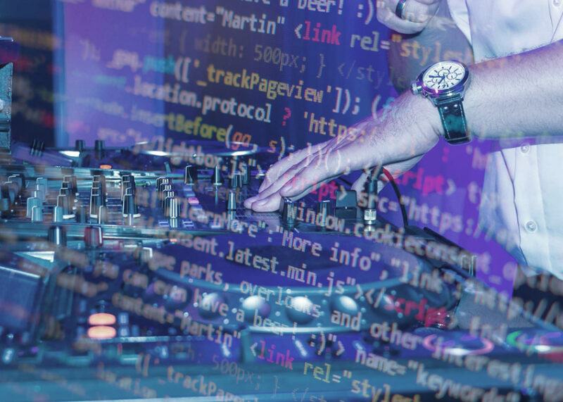 A programmer's hand adjusts DJ turntables while code projections overlay the equipment and workspace.