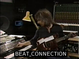 Musician playing synthesizer keyboard in a recording studio with guitar nearby.