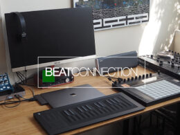 Music producer's desk setup displaying BEATCONNECTION on monitor, featuring keyboard, drum pads, and audio production equipment.