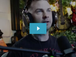 Man wearing large headphones in a music studio with guitars visible in the blurred background.