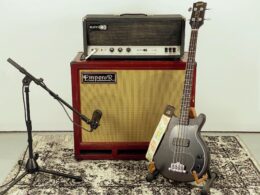 Black bass guitar, red Emperor amplifier with head unit, and microphone stand on speckled surface.