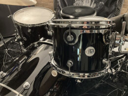 A musician tunes a black DW drum kit featuring multiple toms and polished chrome hardware.