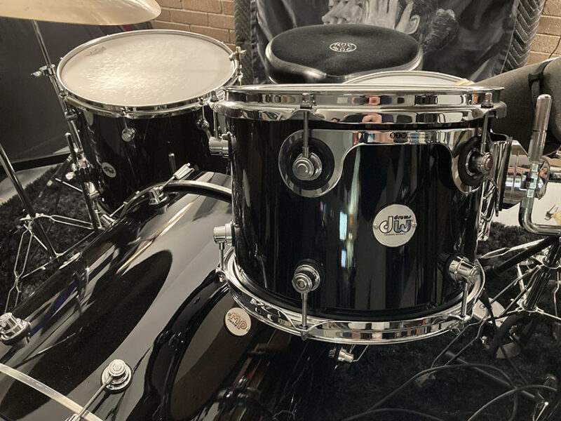 A musician tunes a black DW drum kit featuring multiple toms and polished chrome hardware.