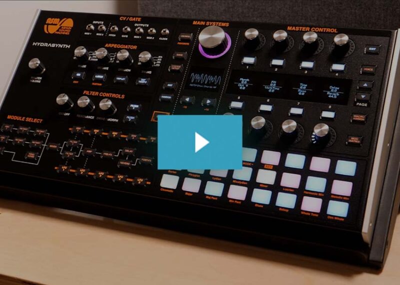 Black ASM synthesizer with orange text labels, numerous knobs, buttons, and a grid of colored pads.