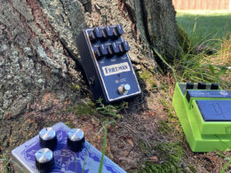 Three guitar effect pedals arranged on the ground outdoors, including a blue Friedman overdrive pedal and two other music gear cases.