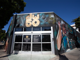 A storefront with a large "50" sign on its awning, featuring colorful murals on its walls beneath a clear blue sky.