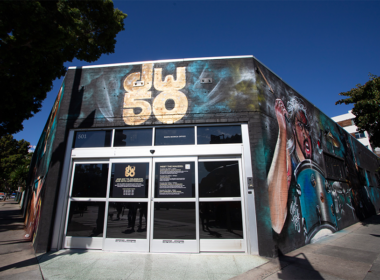 A storefront with a large "50" sign on its awning, featuring colorful murals on its walls beneath a clear blue sky.