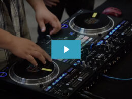 DJ operating dual turntables on an illuminated black mixer setup during a live performance.