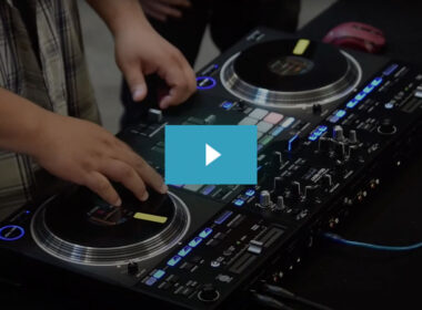 DJ operating dual turntables on an illuminated black mixer setup during a live performance.