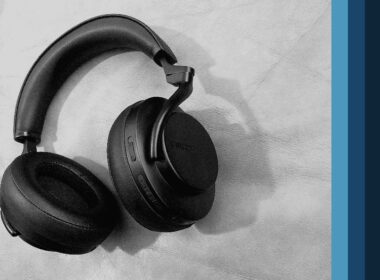 A pair of black over-ear headphones rests against a white textured wall.