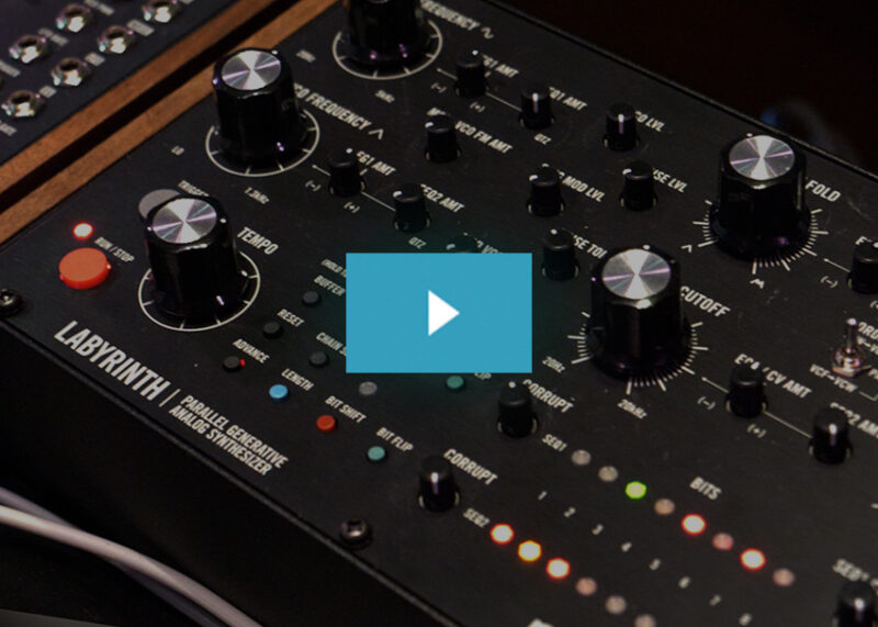 The Moog Labyrinth synthesizer displays multiple black knobs, colored button controls, and a wooden accent panel.