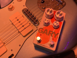 An orange-toned guitar and matching pedal labeled Gary photographed under warm dramatic lighting.