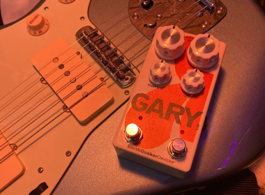 An orange-toned guitar and matching pedal labeled Gary photographed under warm dramatic lighting.