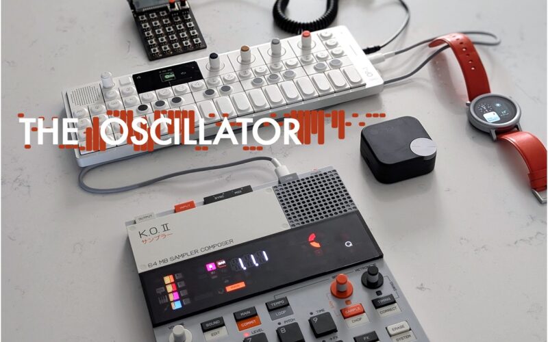 Electronic music production equipment including a white keyboard synthesizer, black sampler, MIDI grid controller, mouse, and smartwatch.