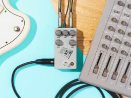 The JHS 424 Gain Stage guitar pedal connects a turquoise guitar to a gray MIDI controller via cables.