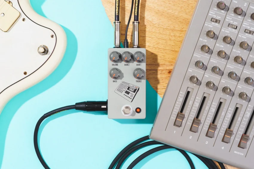 The JHS 424 Gain Stage guitar pedal connects a turquoise guitar to a gray MIDI controller via cables.