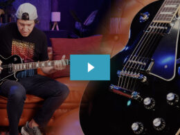 Guitarist plays black electric guitar on red couch in studio with purple and blue lighting.