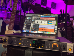 A synthesizer and keyboard controller sit illuminated by purple LED lighting in a professional music studio.