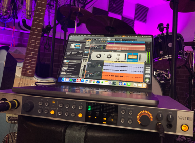 A synthesizer and keyboard controller sit illuminated by purple LED lighting in a professional music studio.