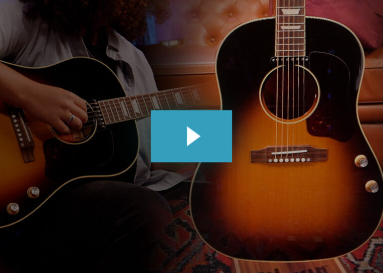 A musician plays a black acoustic guitar next to a larger sunburst acoustic guitar in a warm studio environment.
