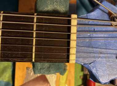 Close-up of a 7-string guitar headstock showing tuning pegs, multiple strings, and part of the fretboard.